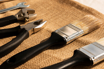 Collection of different mechanic tools laying in a row on brown cloth.