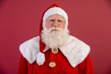 Real Santa Claus with a red background, wearing glasses, gloves and a hat looking camera.