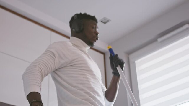 Happy young handsom black man cleaning the flor while listening the music and dancing. High quality 4k footage
