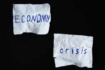 Inscription "Economy crisis" on two crumpled paper sheets against black background. Global world economy collapse concept. Top view