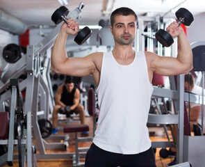 Muscular young man doing exercises with dumbbells at gym