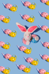 Obraz premium Easter pattern. Repetition of bright Easter eggs on a blue background. In the center of the frame, an Easter bunny toy crawls out of a hole in the paper.