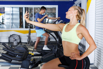 Fototapeta na wymiar young female athlete taking selfie during training in fitness center