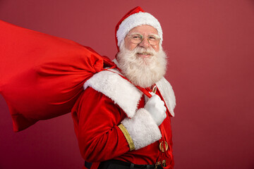 Real Santa Claus with a red background, wearing glasses, gloves and a hat looking side.