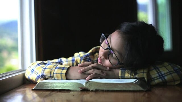 Girl reading bible and fall asleep over wooden table at home. Christian children concept.
