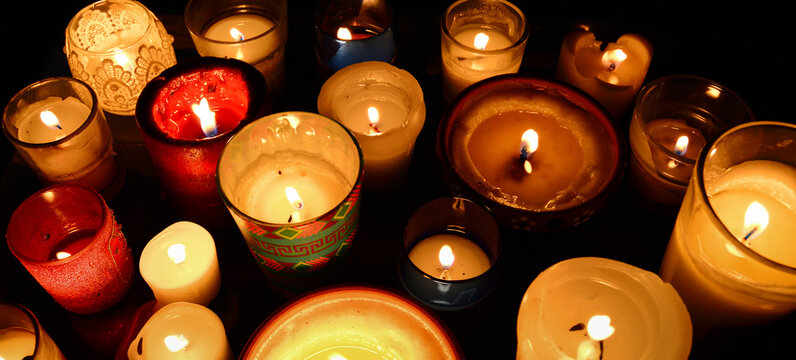 Many candles of different sizes and styles in the dark