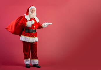 Fototapeta na wymiar Santa Claus pulling huge bag of gifts on red background with copy space. Banner art.