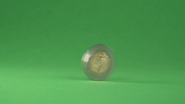 A Mexican 5 pesos coin spinning from right to left on a chroma background.