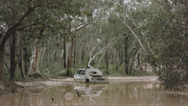Abandoned burnt out car sitting in a puddle on a 4wd outback track.