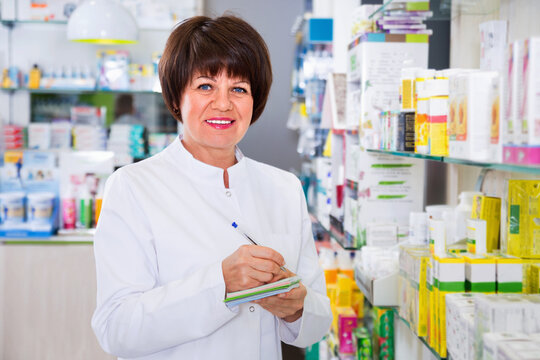 Portrait of cheerful smiling female druggist in white coat working in pharmacy