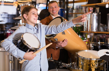 Fototapeta na wymiar happy teenager and father deciding on ethnic drum in musical shop.