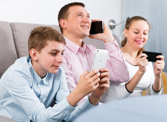 Middle-aged happy family playing with their smartphones together at home