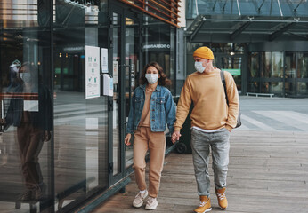 Stylish young family couple hipsters in face mask against the glass building, new normal