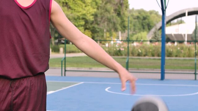 Teenager plays with basketball on playground outdoor. Guy bangs ball on floor. Ball and guy's torso close up. Slow motion.
