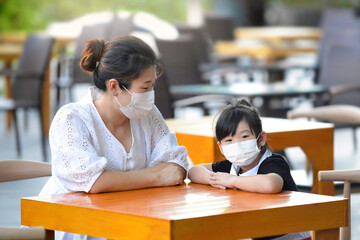 Chinese Asian mother and child with mask waiting to be served in restaurant setting.People with facemask in outdoor table wait for service.Social distancing SOP with facemasks.