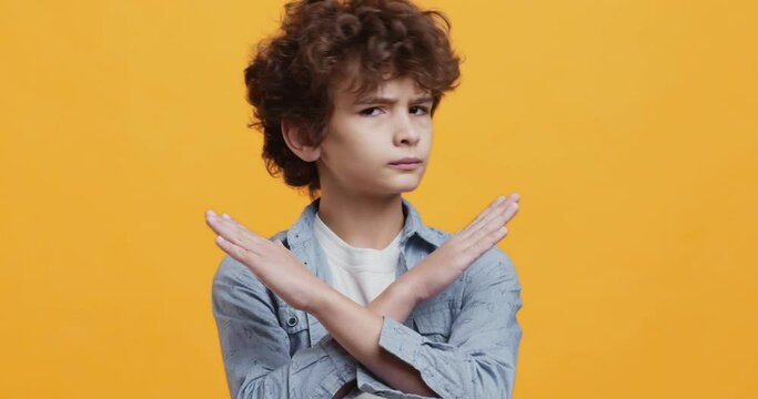 Stop children abuse. Cute curty boy gesturing no, crossing hands and shaking head, expressing reject and denial