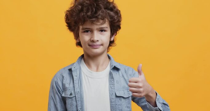 Children approval. Adorable curly little boy nodding head and showing thumb up gesture, agreement and like concept