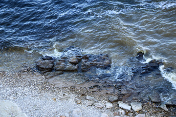 waves run onto the shore and crash against the rocks, creating many splashes and splashes near the shore. river surf in stormy weather near a stone pebble coast with foamy splashing waves.