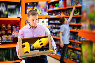 Portrait of glad cheerful positive adult man buying toy cement mixer machine in modern toy store