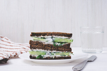 sandwich with black bread, cucumber and cream cheese on a plate on white background. vegetarian food concept