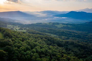Fototapeta premium Early morning in the mountains. Morning sun and haze in the valley against the background of mountains. Green fields and meadows. Adygea, Russia