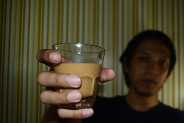 a glass of coffee milk in the right hand of an Asian man