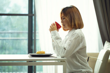 Asian woman's hand holding a red cup of coffee.Enjoing morning with cup of coffee