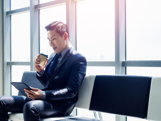 Good looking Asian businessman in suit with tablet.