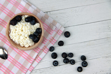 wooden bowl of farmer cheese on red and white napkin and a pile of blueberry on white wooden background flat lay. Healthy eating concept. Horizontal image