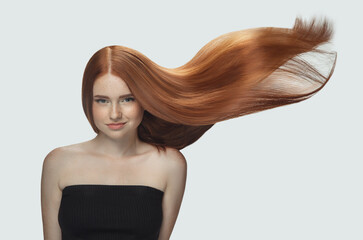 Beautiful model with long smooth, flying red hair isolated on white studio background. Young caucasian girl with well-kept skin and hair blowing on air. Concept of salon care, beauty, fashion.