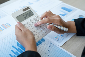 The hand of an accountant woman is analyzing and calculating the financial graph showing the results in the office
