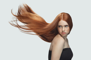 Beautiful model with long smooth, flying red hair isolated on white studio background. Young...