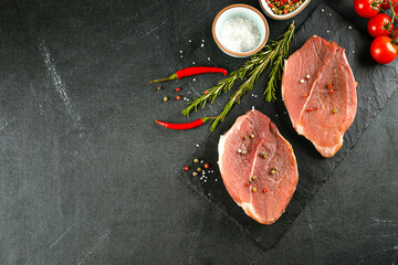 Raw meat, pork steaks with spices, herbs on board on dakr table background. Copy space, top view