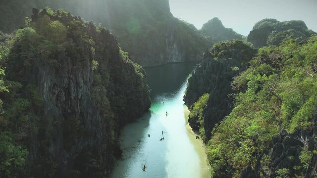 Green forest at mountain banks of tropic river with boats aerial. Summer cruise on passengers vessels at tropical stream with cliff shore. Philippines paradise vacation at ocean bay with azure water