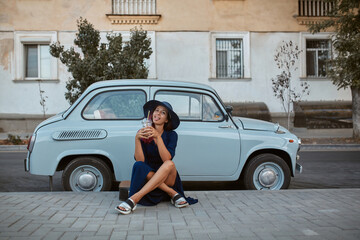 Pretty woman enjoy drink sitting near blue old fashioned car. Fun and spare time. Street style and city walk concept
