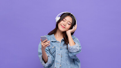 Young happy Asian girl wearing headphones listening to music from mobile phone with eyes closed on...