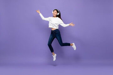 Fototapeta na wymiar Young happy pretty Asian girl wearing headphones and jumping on isolated purple studio background