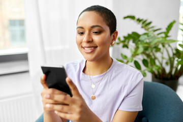 technology and people concept - smiling african american woman in glasses with smartphone at home