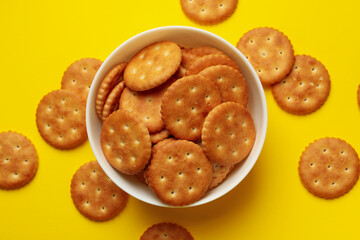 Wooden bowl with tasty cracker biscuits on yellow background