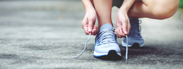 Running shoes. close up female athlete tying laces for jogging on road. Runner ties getting ready for training. Sport lifestyle. copy space banner. - obrazy, fototapety, plakaty