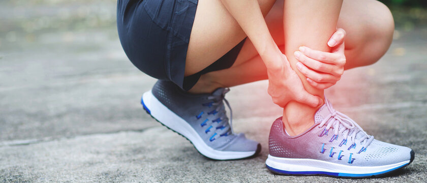 Runner female touching painful twisted or broken ankle. Athlete training accident. Sport sprain cause injury knee leg bones while run in outdoor the park. 