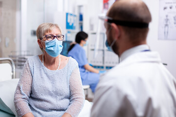 Sick old woman wearing protective mask during consultation for coronavirus outbreak in hospital...
