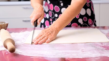 Obraz na płótnie Canvas female hands roll out the dough with a rolling pin on a wooden surface, close-up. female hands rolling dough on a lilac table. Chef hands stroking the dough. Hands roll out the dough with a rolling