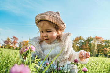 Caucasian child girl sitting in the grass surrounded by flowers clovers