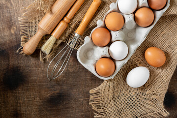 Eggs in a tray on the kitchen table. White and brown eggs with a whisk and rolling pin. Chicken eggs and whisk on a culinary background. Concept of preparation for baking. Top view with copyspace