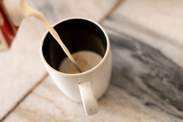 pouring milk into coffee cup mug white marble natural light background