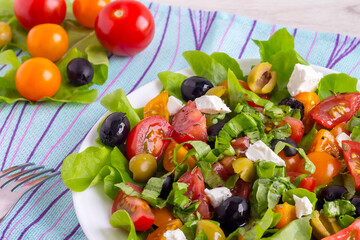 Fototapeta na wymiar Fresh vitamin vegetable salad with tomatoes, olives, feta, lettuce on a white plate for a healthy diet.