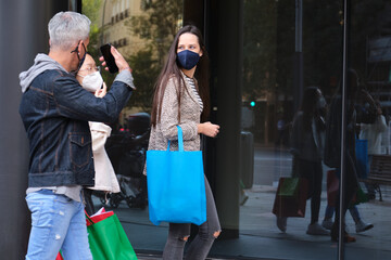 Three friends wearing face mask talking and walking on street carrying shopping bags. Shopping during pandemic times.