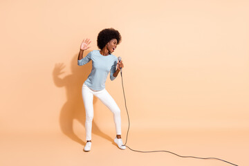 Photo portrait of dark skin woman singing in karaoke holding mic in one hand isolated on pastel beige colored background