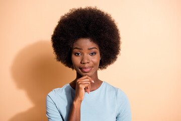 Photo portrait of successful african american woman touching chin with one finger isolated on pastel beige colored background